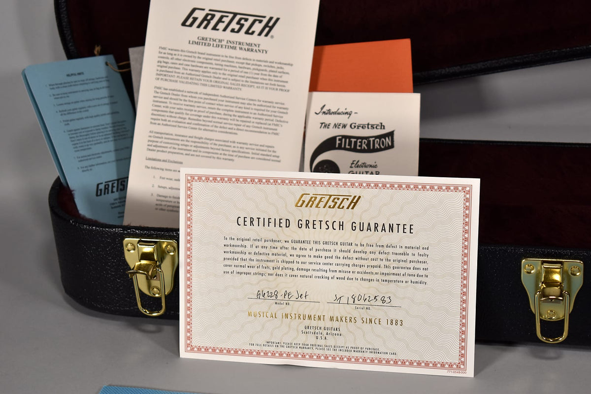 A close-up of the guitar's open black hard case, revealing a gold-stamped guarantee certificate and other paperwork.