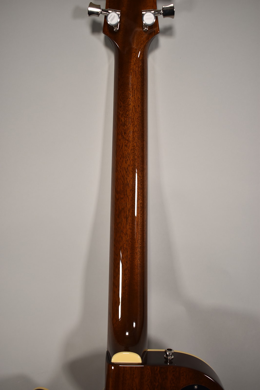 The guitar's glossy dark brown neck and headstock are viewed from the back, showing chrome tuners and a cream heel cap.