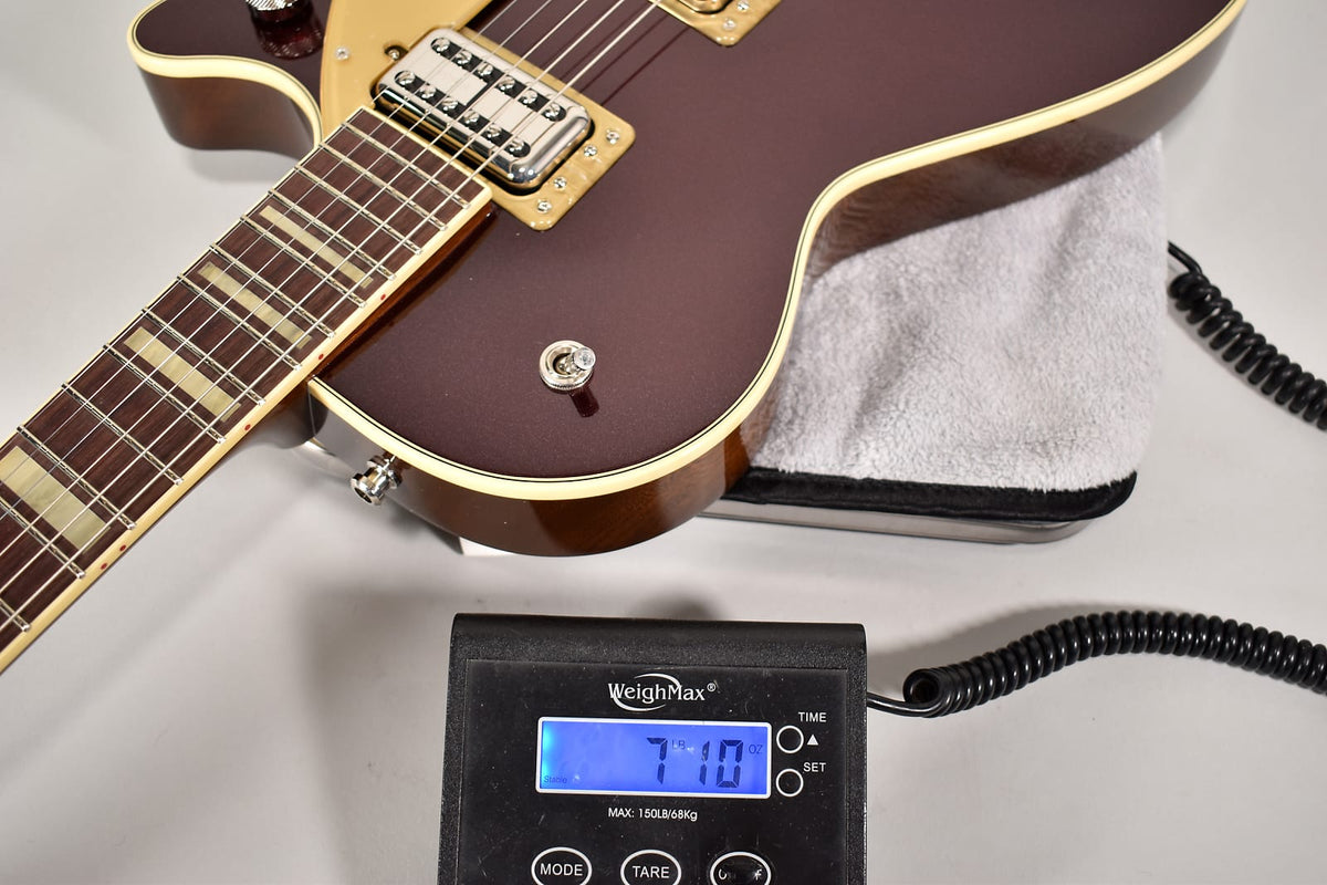 The deep metallic red guitar with cream binding rests on a scale displaying 7lb 10oz, showing its lower bout and neck.