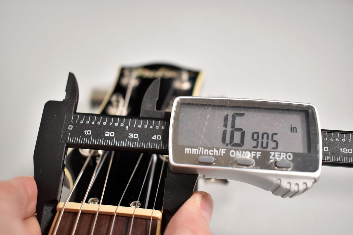 A digital caliper measures the nut width of the dark-finished guitar neck at 1.6905 inches, with a bone nut and rosewood fretboard visible.