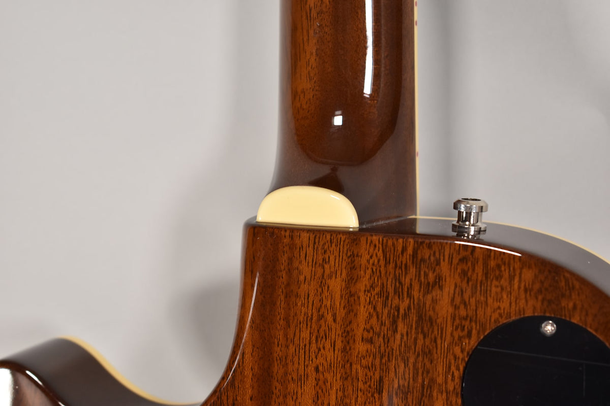 Close-up of the guitar's glossy dark brown neck heel and body, showing a cream neck binding and a chrome strap button.