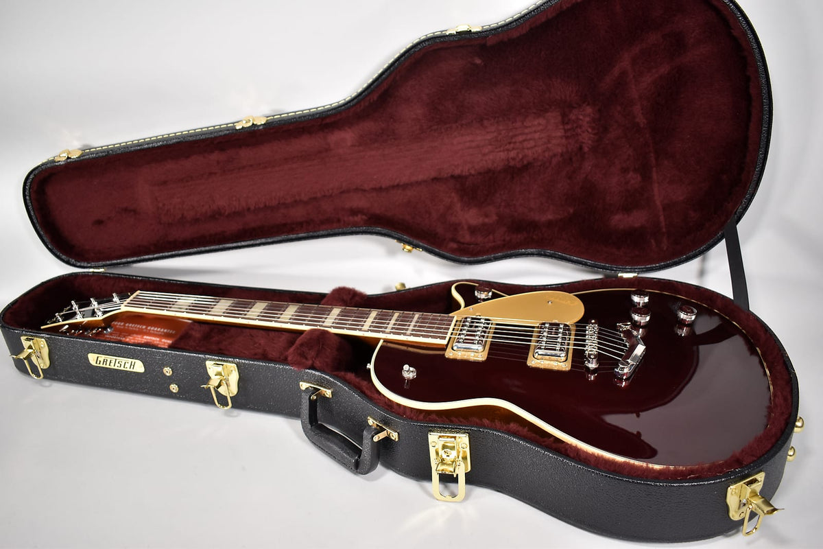 Dark red electric guitar with a gold pickguard and chrome hardware, resting in a black hard case with a burgundy plush interior.