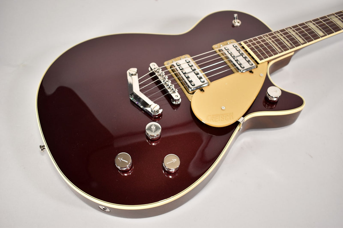 The dark red sparkle electric guitar body, with cream binding, chrome hardware, and a gold pickguard, is angled from the lower right.