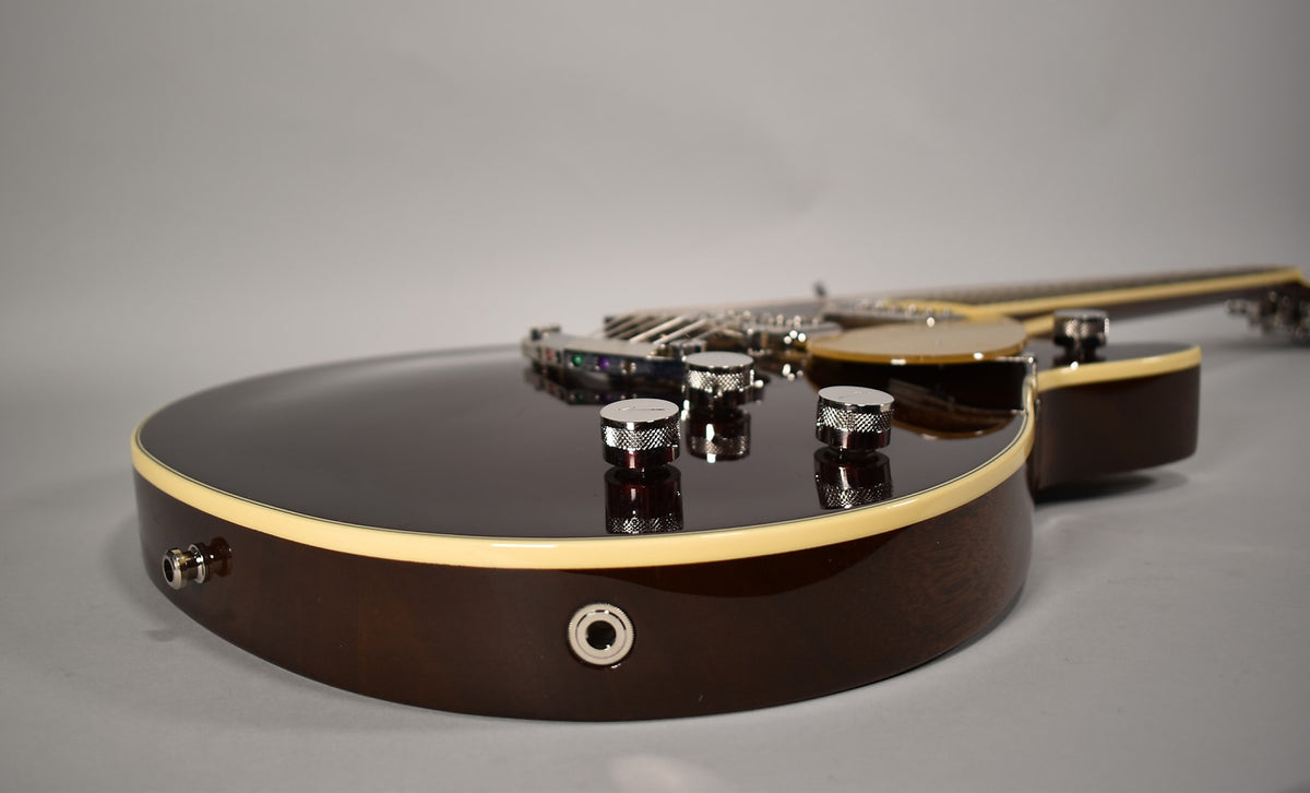 The guitar's dark brown body, with cream binding, is angled from the lower left, showing three chrome knurled control knobs.