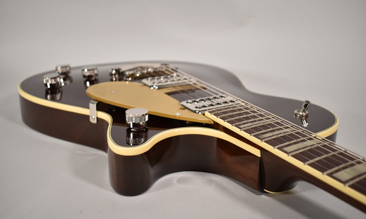 Upper body of a dark brown electric guitar, showing the gold pickguard, chrome hardware, and cream binding.