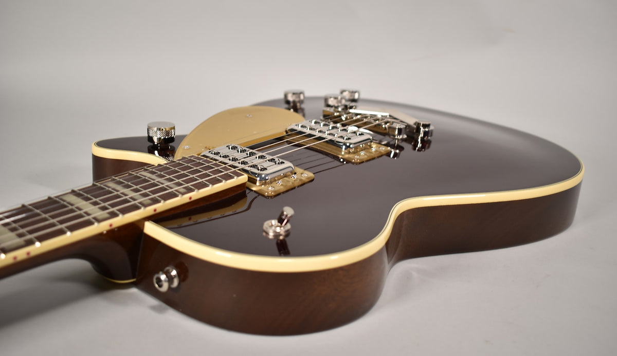 Close-up of a dark brown electric guitar with cream binding, gold pickguard, and chrome hardware, angled from the neck to the body.