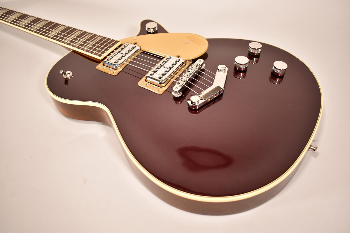 A dark red electric guitar with a cream pickguard and chrome hardware, viewed from above, showing the body and lower neck.