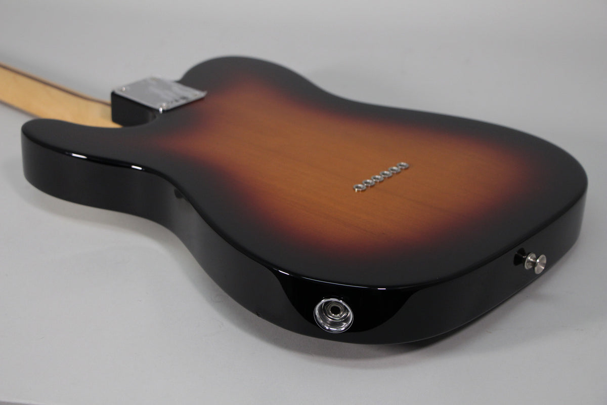 The back of a glossy sunburst Telecaster body, angled from the lower bout, showing the string-through ferrules and input jack.