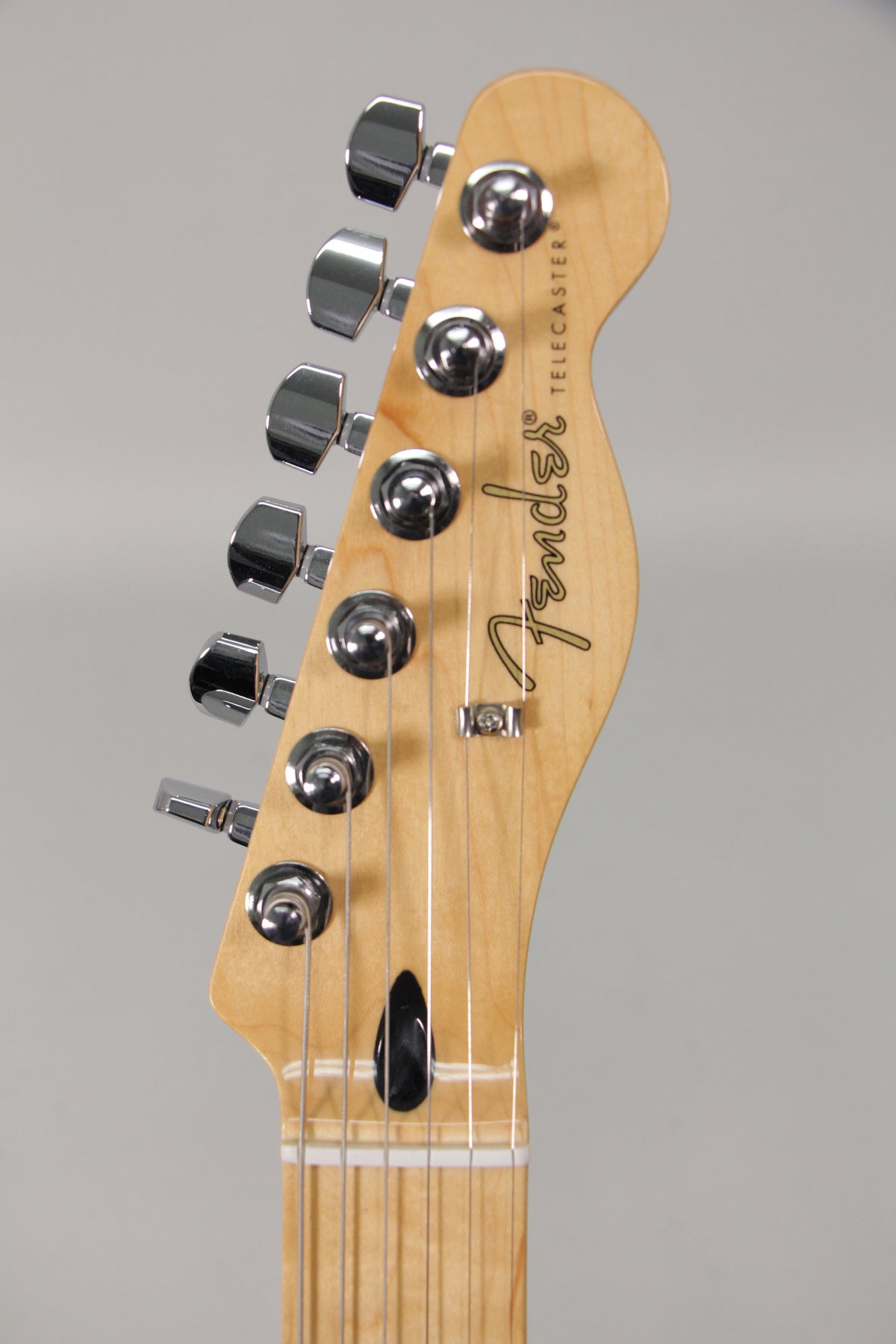 Close-up of the light wood headstock and top of the neck, showing six chrome tuners and a black string tree.