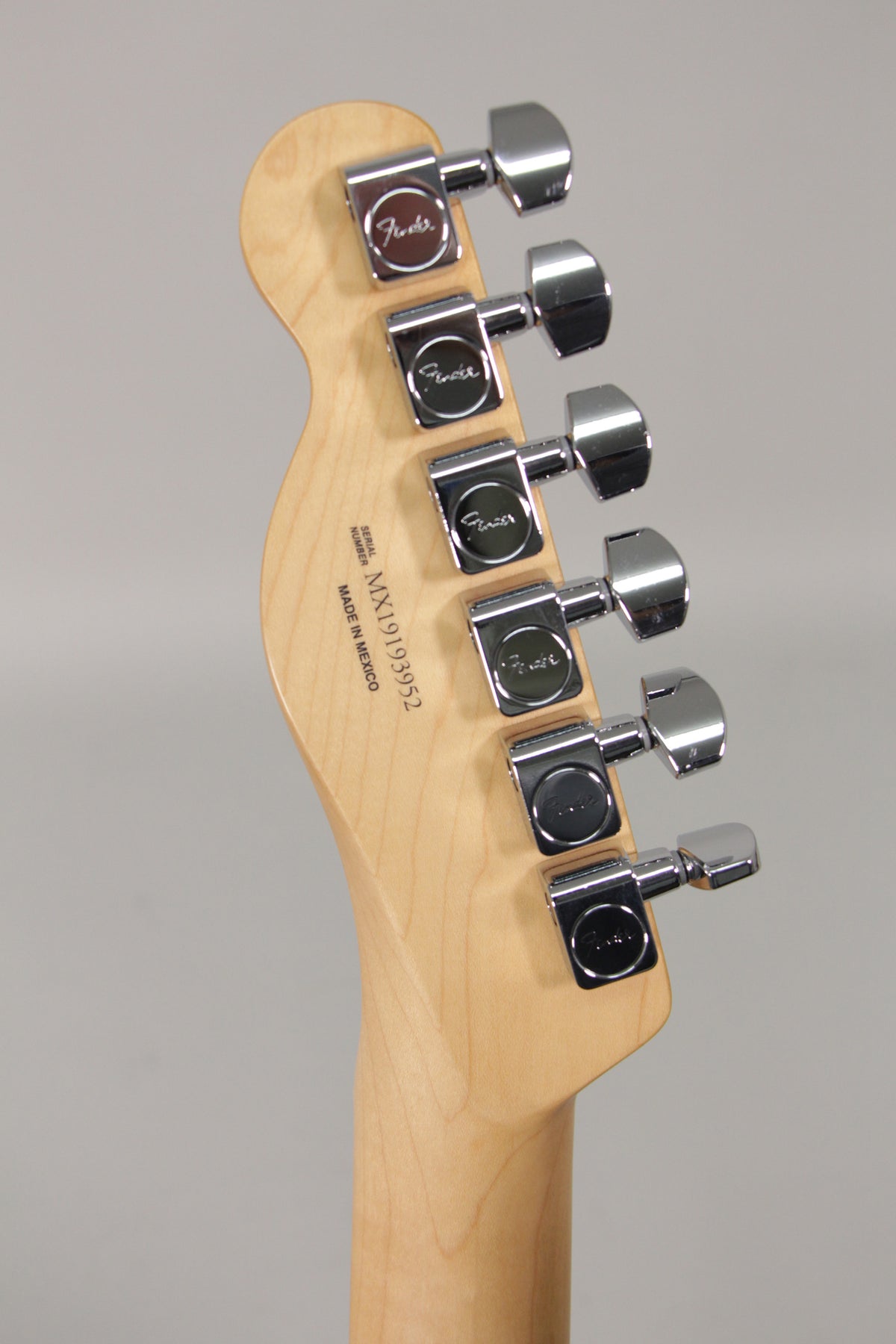 The back of the guitar's light maple headstock and neck, with six chrome tuners visible, angled slightly from the left.