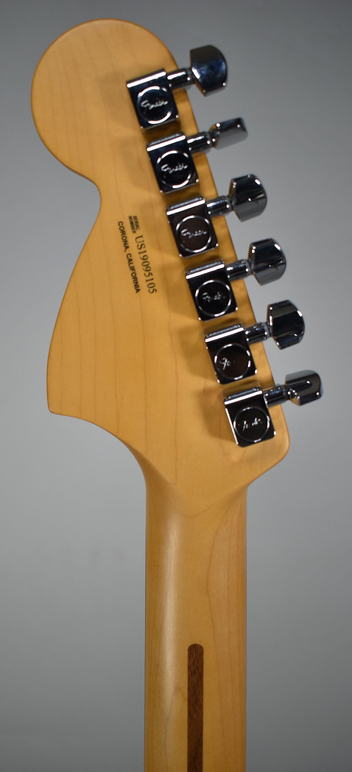 The back of a light maple headstock and neck, angled slightly left, showing six chrome tuners and a dark wood skunk stripe.