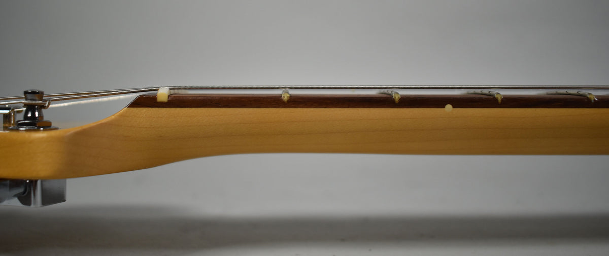 The guitar's light-colored neck and dark fretboard are seen from the side, with a string tree and nut visible near the headstock.