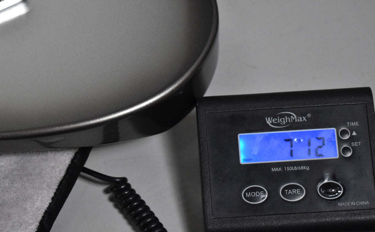 The Mercury finish guitar body rests on a scale displaying "7.12" lbs, with a coiled cable visible below.