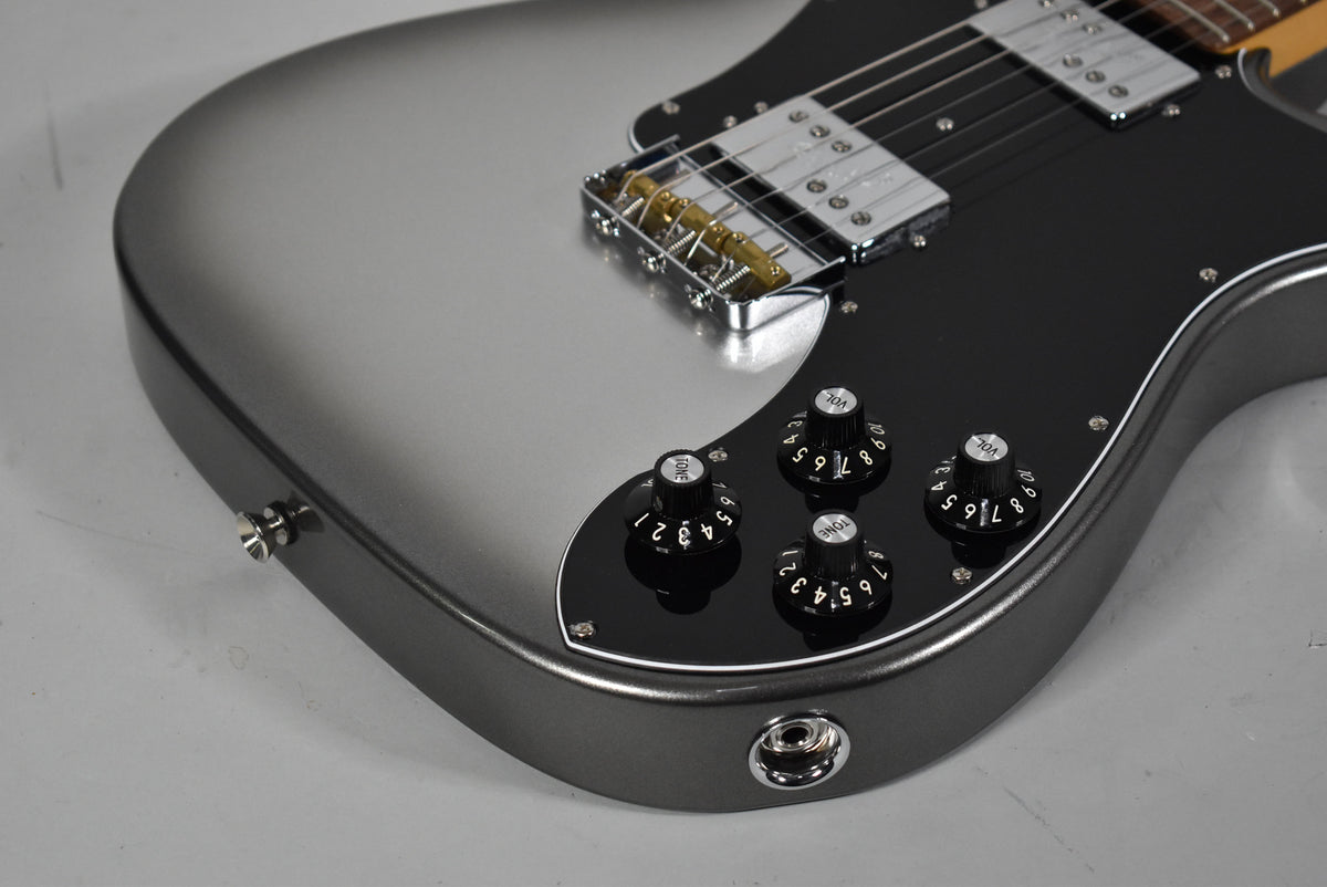 Close-up of the lower bout of a grey burst guitar, showing the black pickguard, two humbuckers, and four black control knobs.