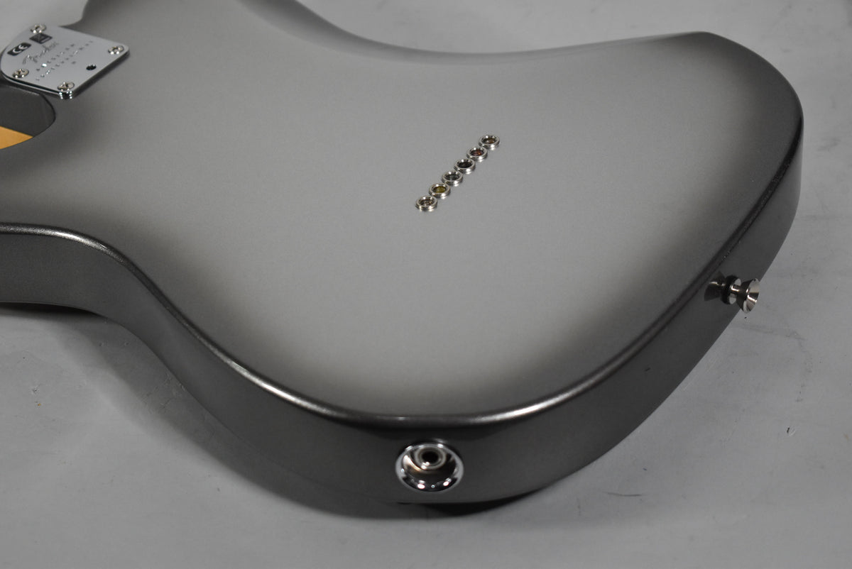 The back of a gray Telecaster body, showing the neck plate, string ferrules, and output jack.