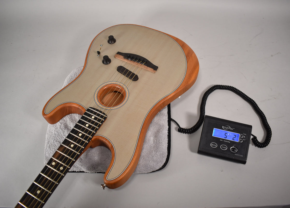 Acoustic-electric guitar with light wood top, brown sides, and dark fretboard, resting on a towel next to a scale displaying "5.2".