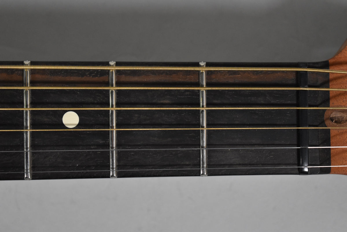Close-up of the dark fretboard with gold strings, showing a single white dot inlay on the 7th fret and light wear on the frets.