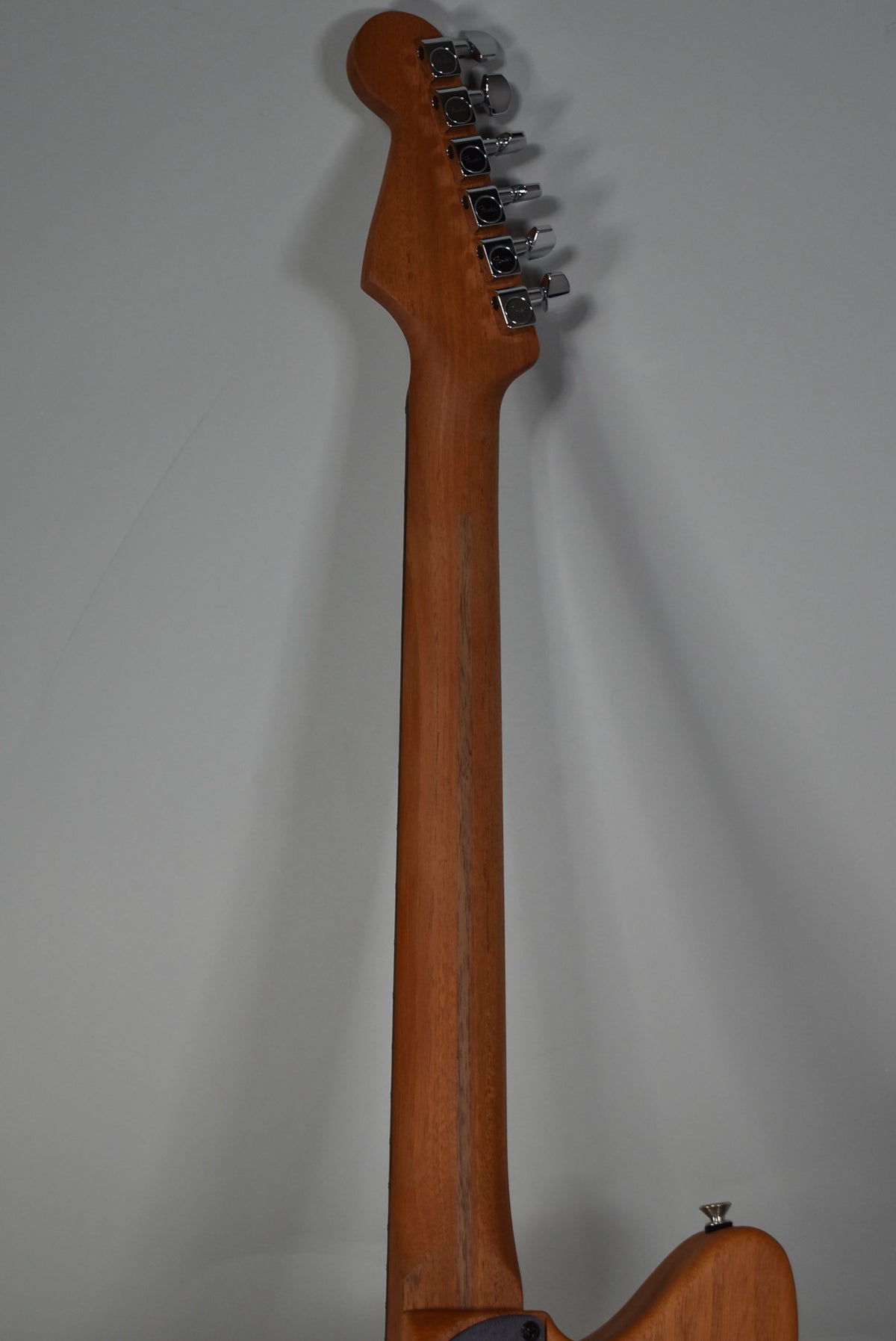 The back of the guitar's light brown neck and headstock, with six chrome tuners, is shown against a plain gray background.