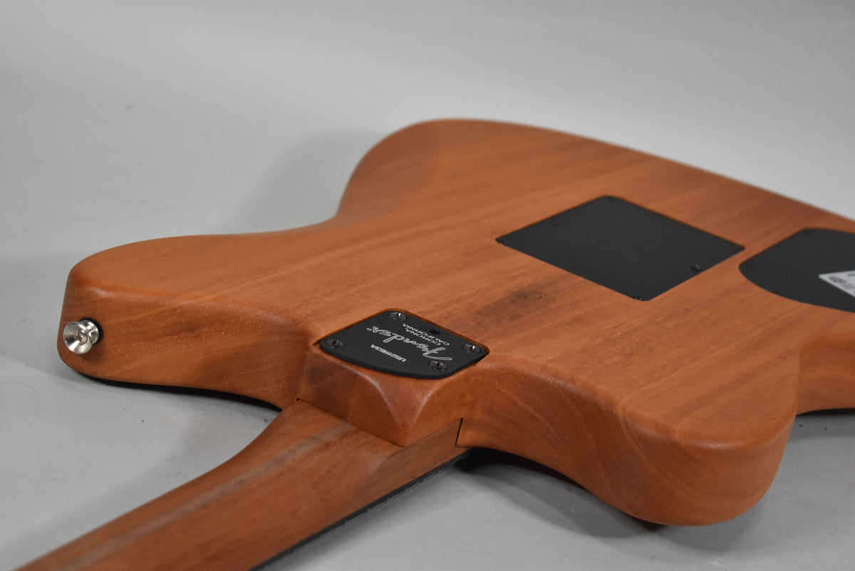 The back of a light brown wooden guitar, showing the neck joint, output jack, and two black control cavity covers.