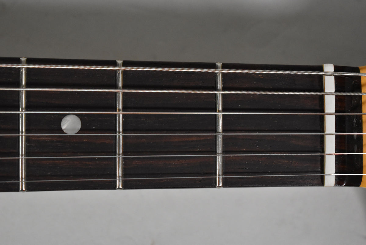 Close-up of the dark fretboard with silver frets and strings, showing a single round mother-of-pearl inlay at the 3rd fret.