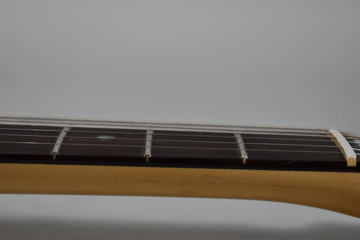 Close-up of the guitar's neck and dark fretboard from the side, showing the first few frets and a cream-colored nut.