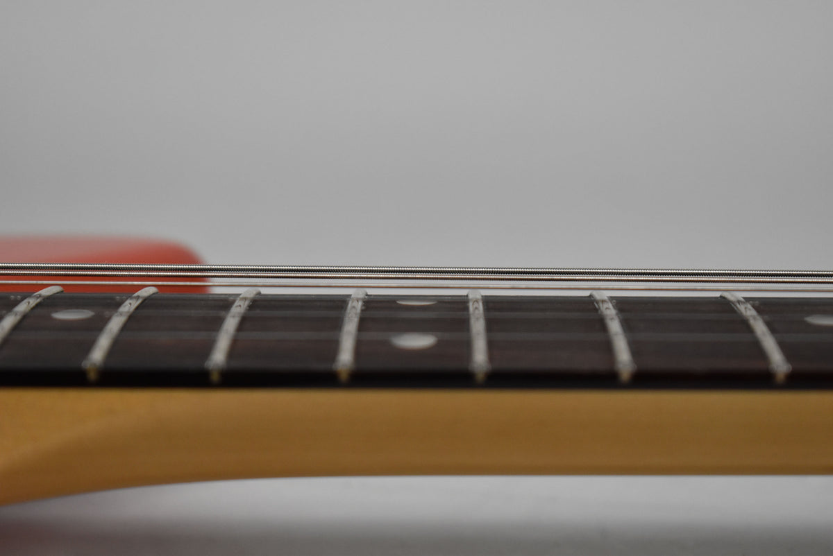 Close-up of the guitar's dark fretboard with white dot inlays and metal frets, showing the strings running above.