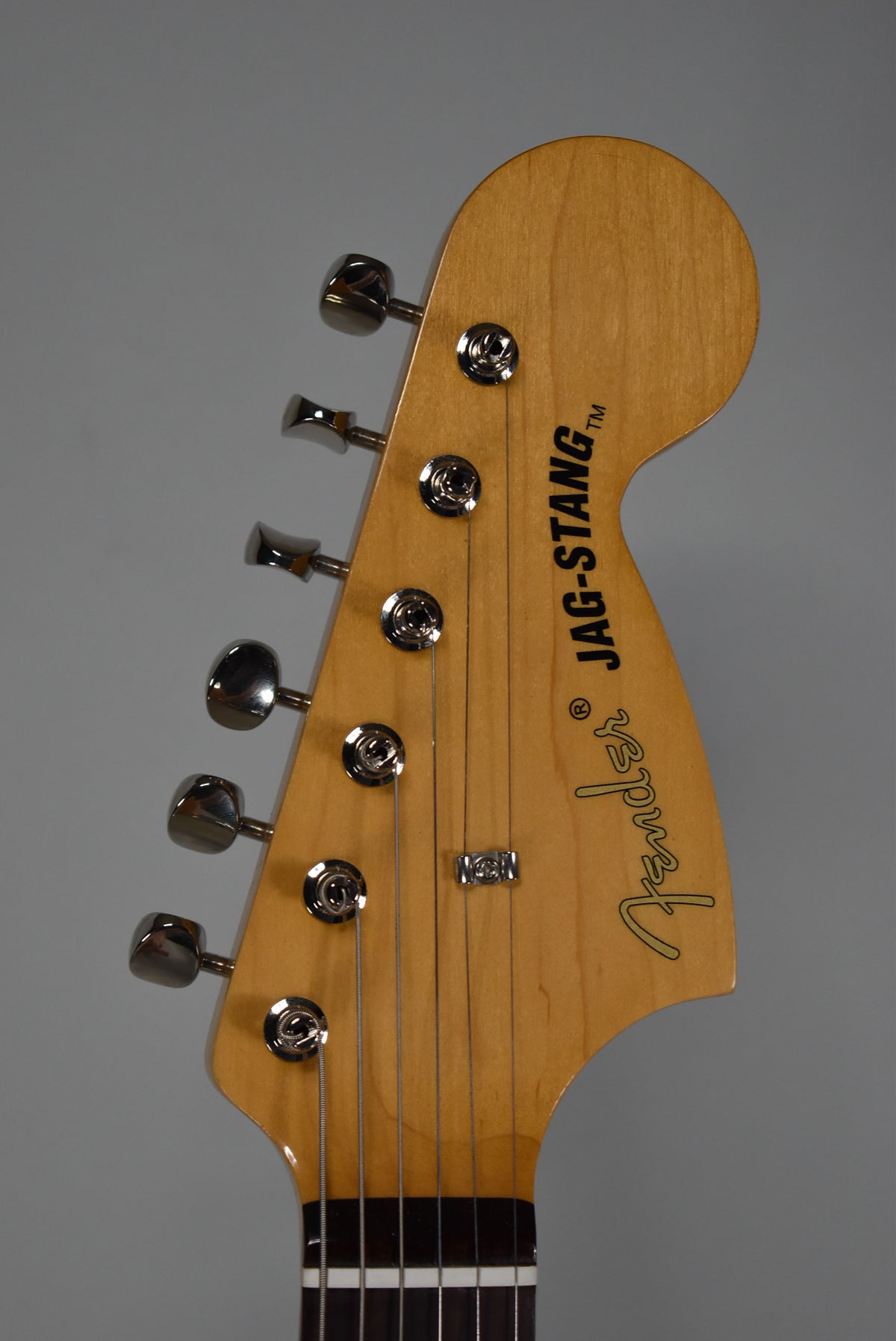 The guitar's light brown headstock, angled slightly left, features six chrome tuners and a string tree, with a dark fretboard visible below.