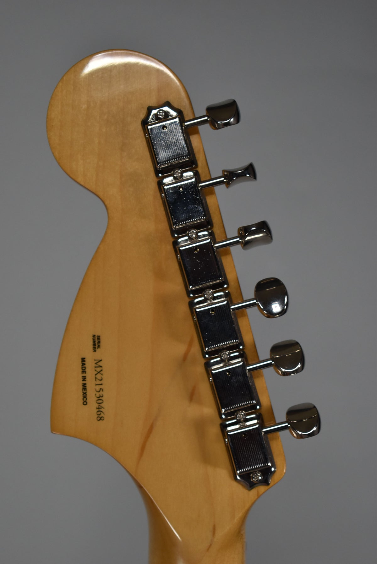 The back of the guitar's light-colored headstock, with six chrome tuners, is angled slightly to the left.