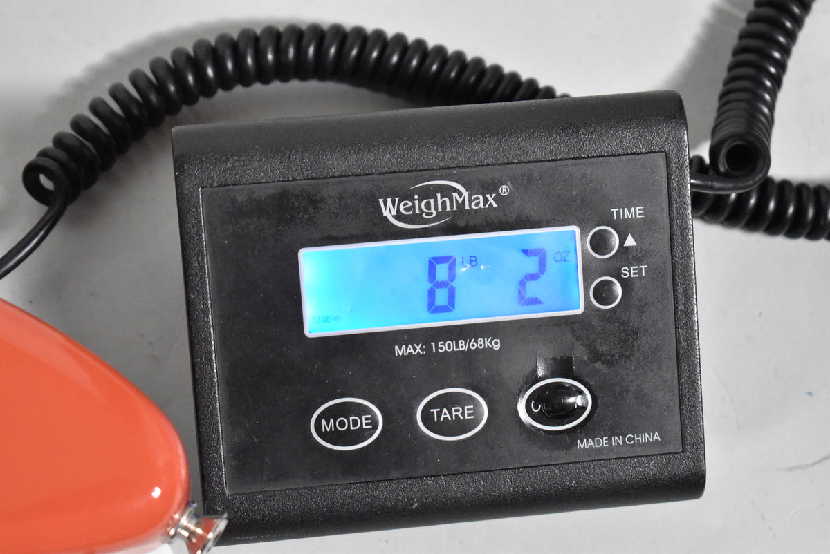 A black digital scale displays "8 LB. 2 OZ." with a coiled black cable and a small part of the red guitar body visible.