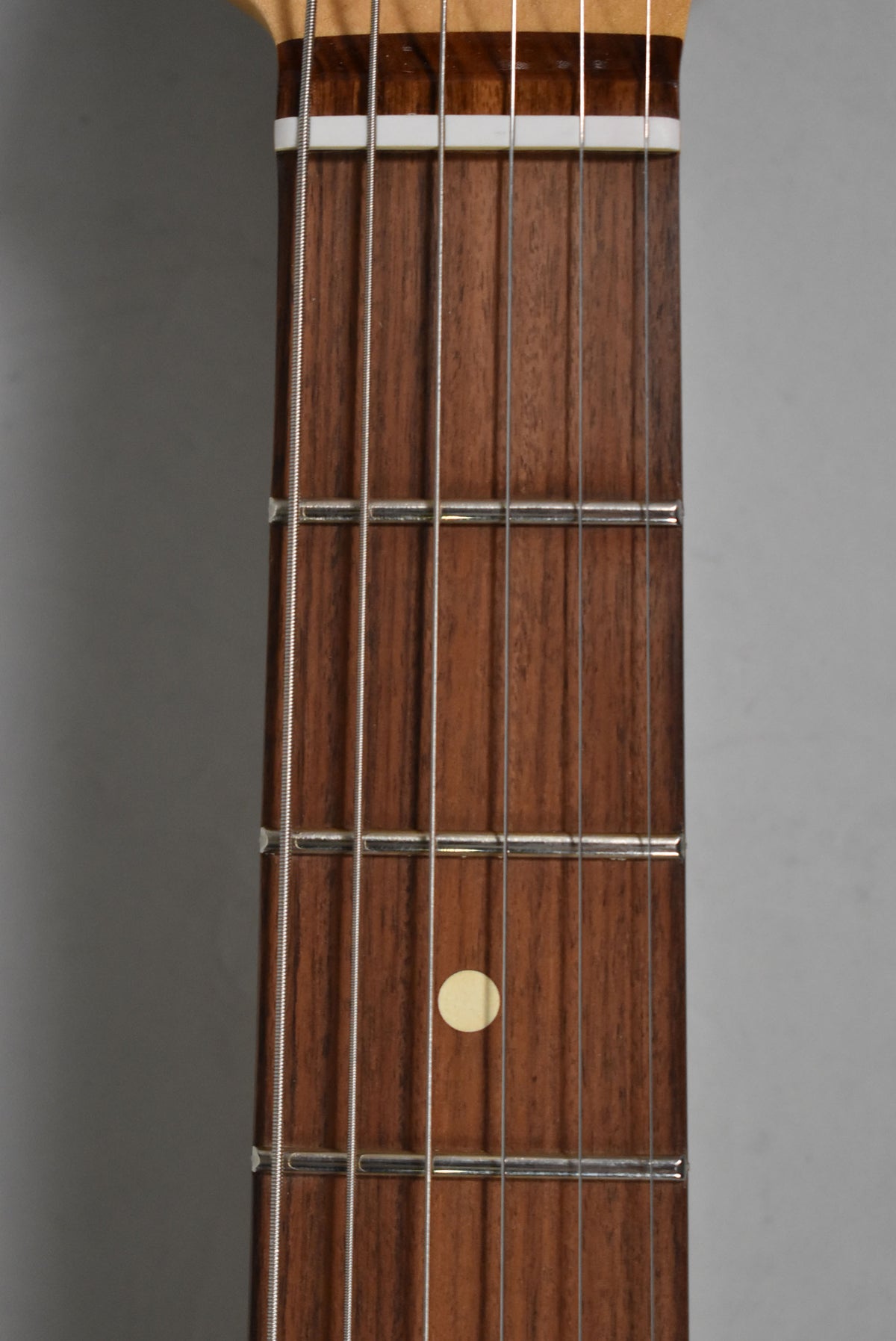 Close-up of the guitar's dark wood fretboard, showing six strings, metal frets, and a single cream-colored dot inlay at the 7th fret.