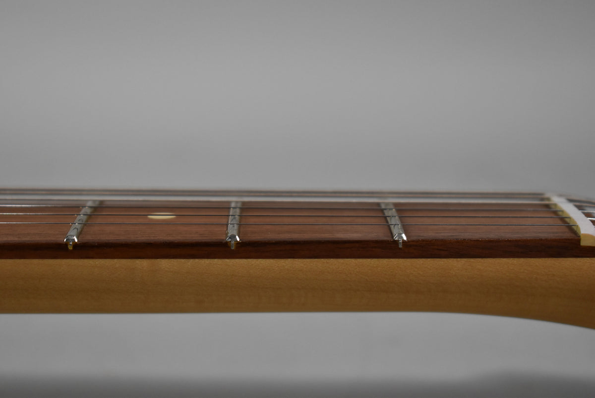 Close-up of the guitar's dark rosewood fretboard and light maple neck, showing the first five frets and a single dot inlay.