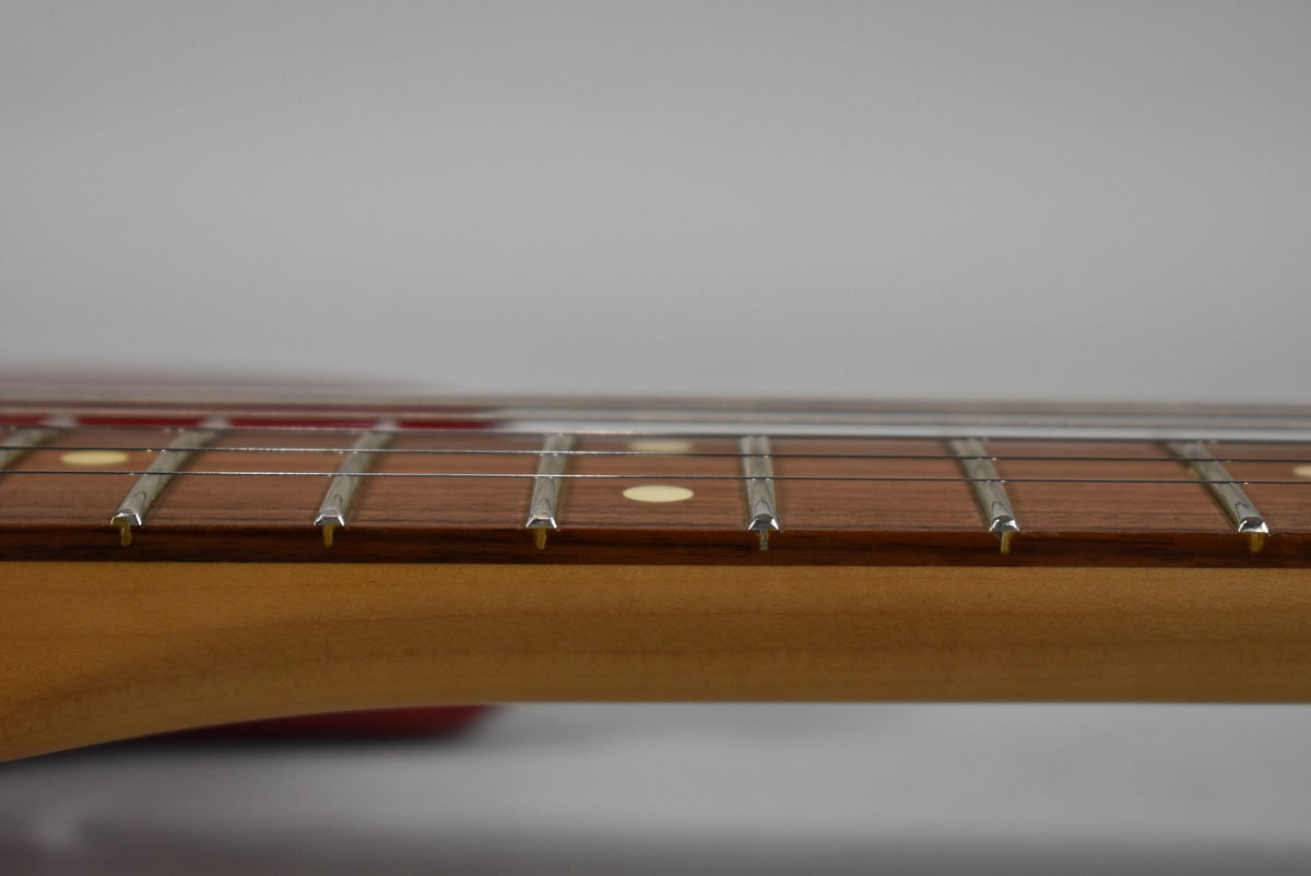Close-up of the guitar's neck and fretboard from the side, showing the light brown wood, frets, and dot inlays.