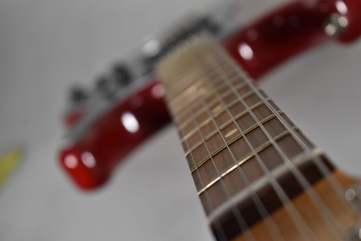 A close-up of the guitar's dark fretboard and frets, with the glossy crimson body blurred in the background.