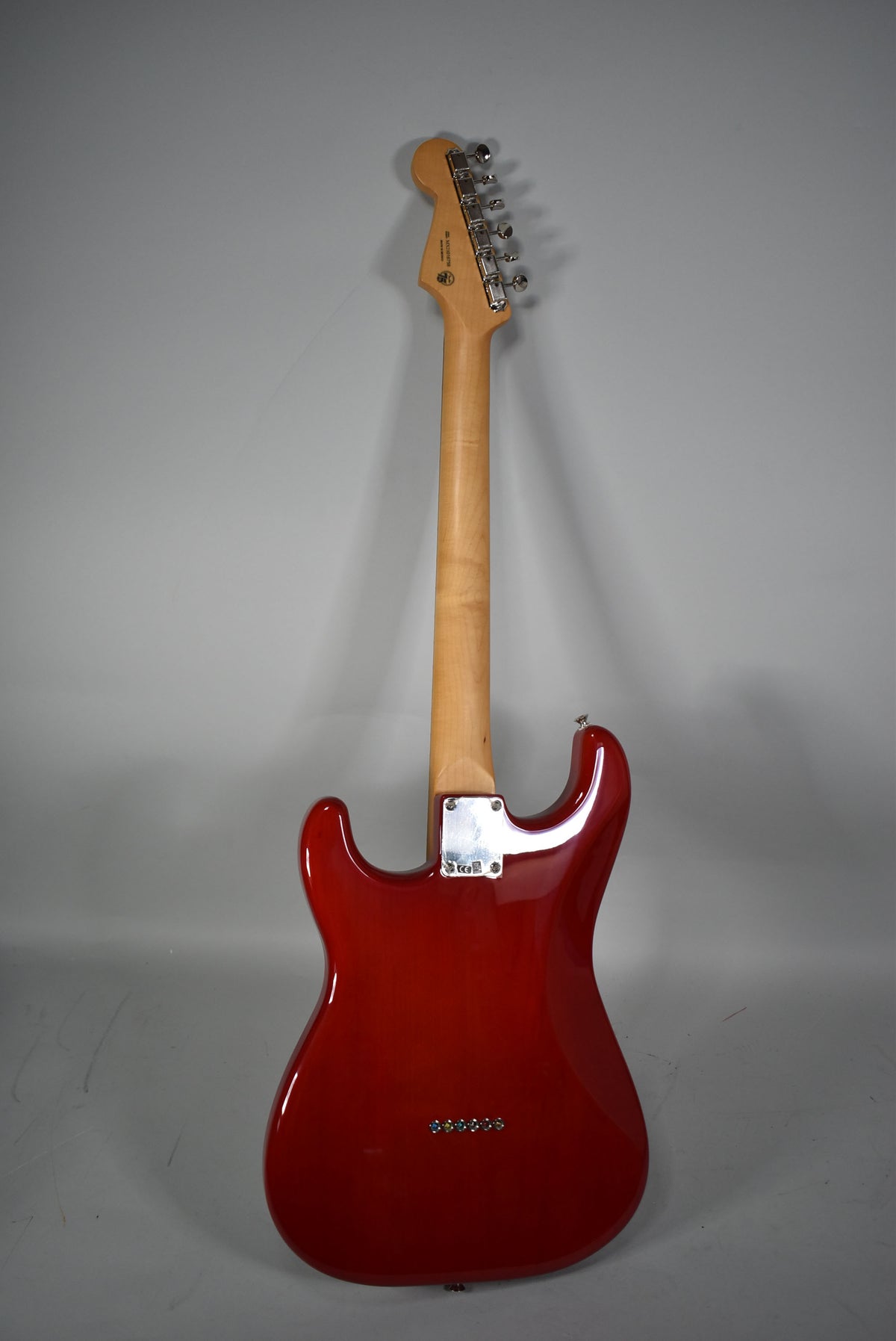 Full rear view of a glossy crimson red Stratocaster with a light maple neck, chrome tuners, and string-through-body bridge.