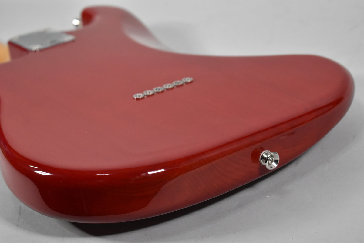 The guitar's crimson red body, with visible wood grain, is angled to show the back, six string ferrules, and output jack.