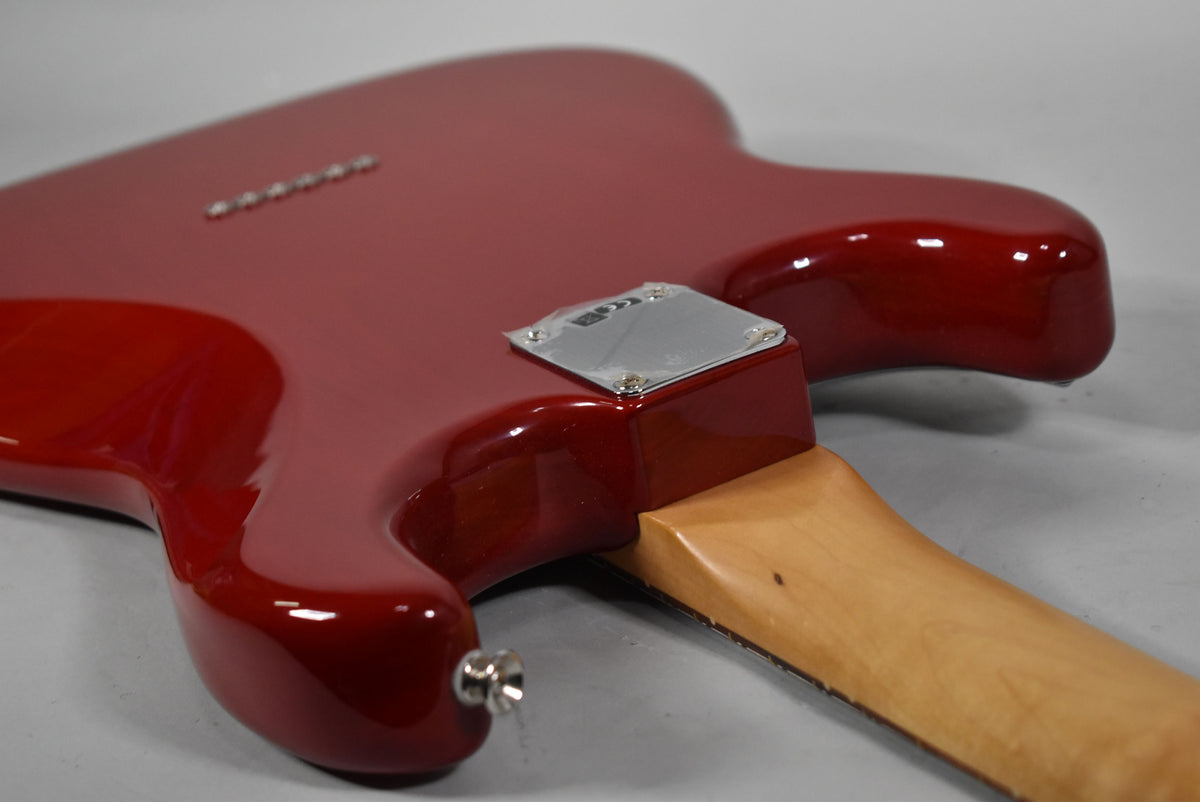 The crimson red guitar body, with a glossy finish, shows a chrome neck plate and string-through-body ferrules, with a light wood neck.