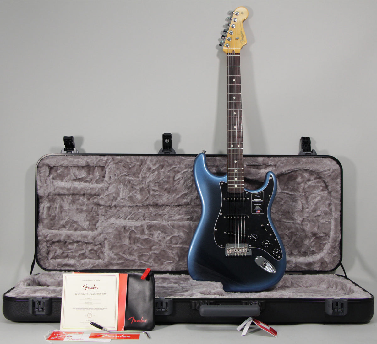 Dark blue Stratocaster guitar with black pickguard, open hard case, certificate of authenticity, and accessories.