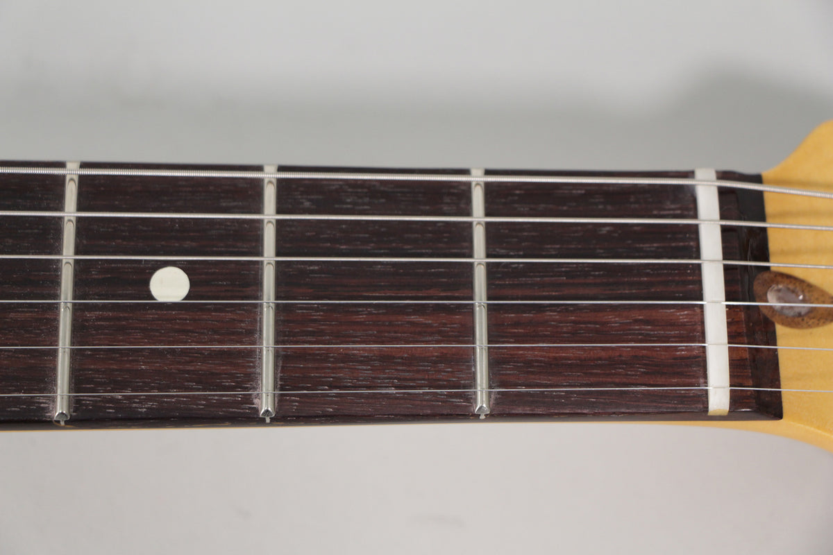 Close-up of the dark rosewood fretboard with silver frets and a white dot inlay at the 7th fret, angled from the treble side.