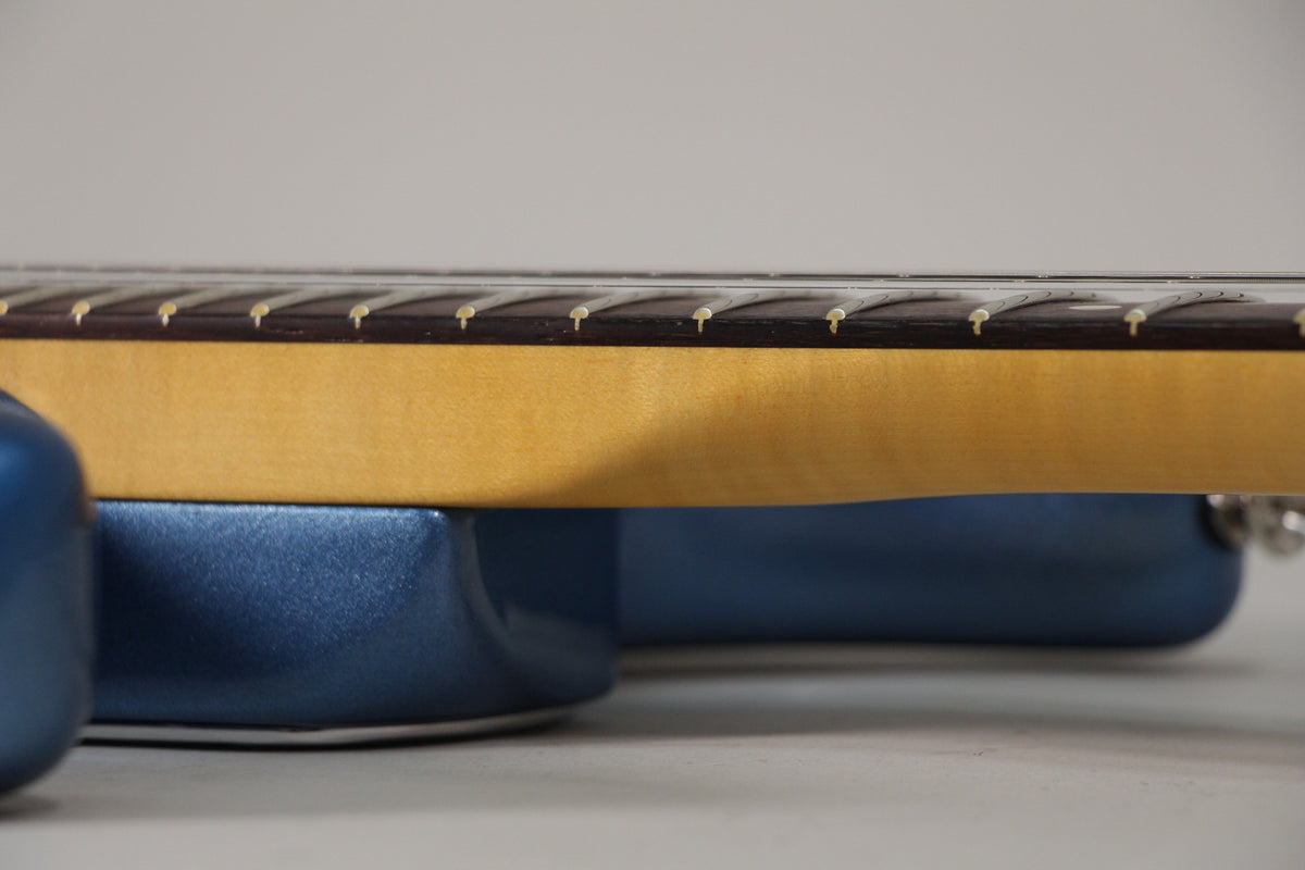 Close-up of the guitar's dark blue metallic body and light wood neck, showing the fretboard with white dot inlays and frets.