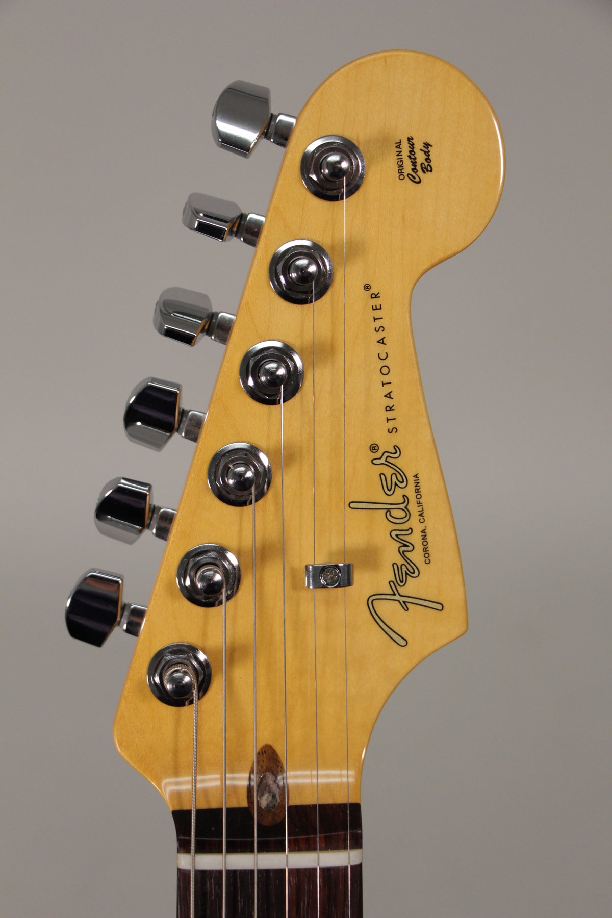 Close-up of the light maple headstock, angled left, showing six chrome tuners, a string tree, and the top of the dark fretboard.