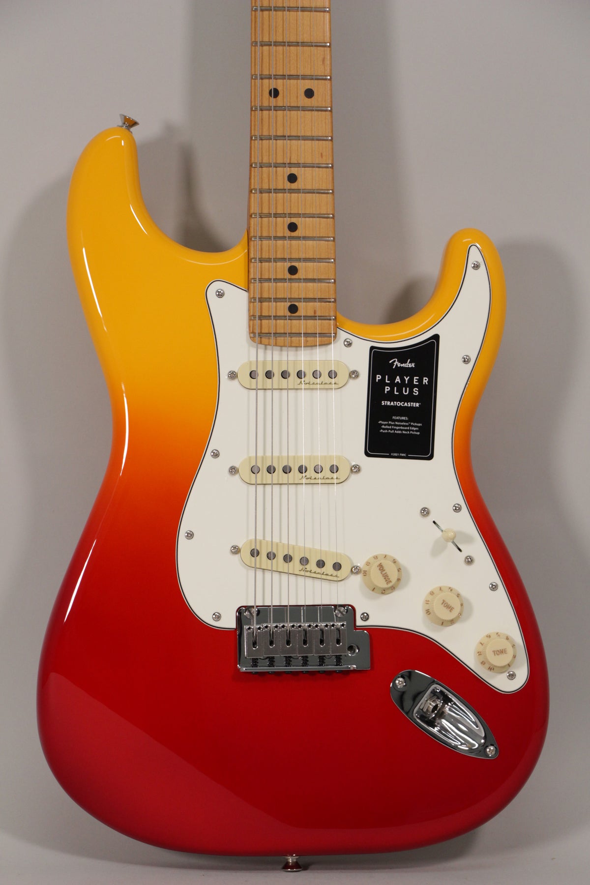 Full-frame view of a glossy red-to-yellow sunburst Stratocaster with a white pickguard, three cream single-coil pickups, and a maple fretboard.