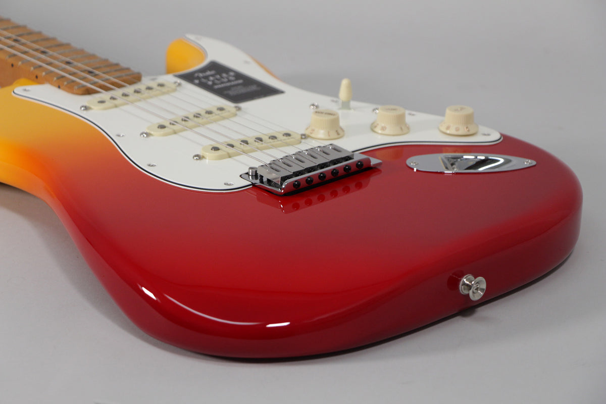 Close-up of a glossy red-to-yellow burst Stratocaster body with a white pickguard, three cream single-coil pickups, and chrome hardware.