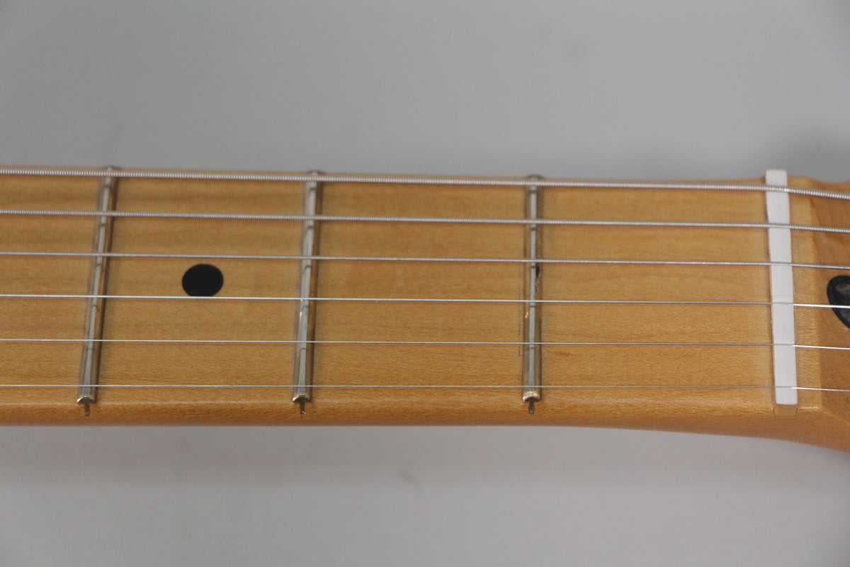 Close-up of the maple fretboard with six strings, showing frets 1-5, a black dot inlay on the 3rd fret, and a white nut.