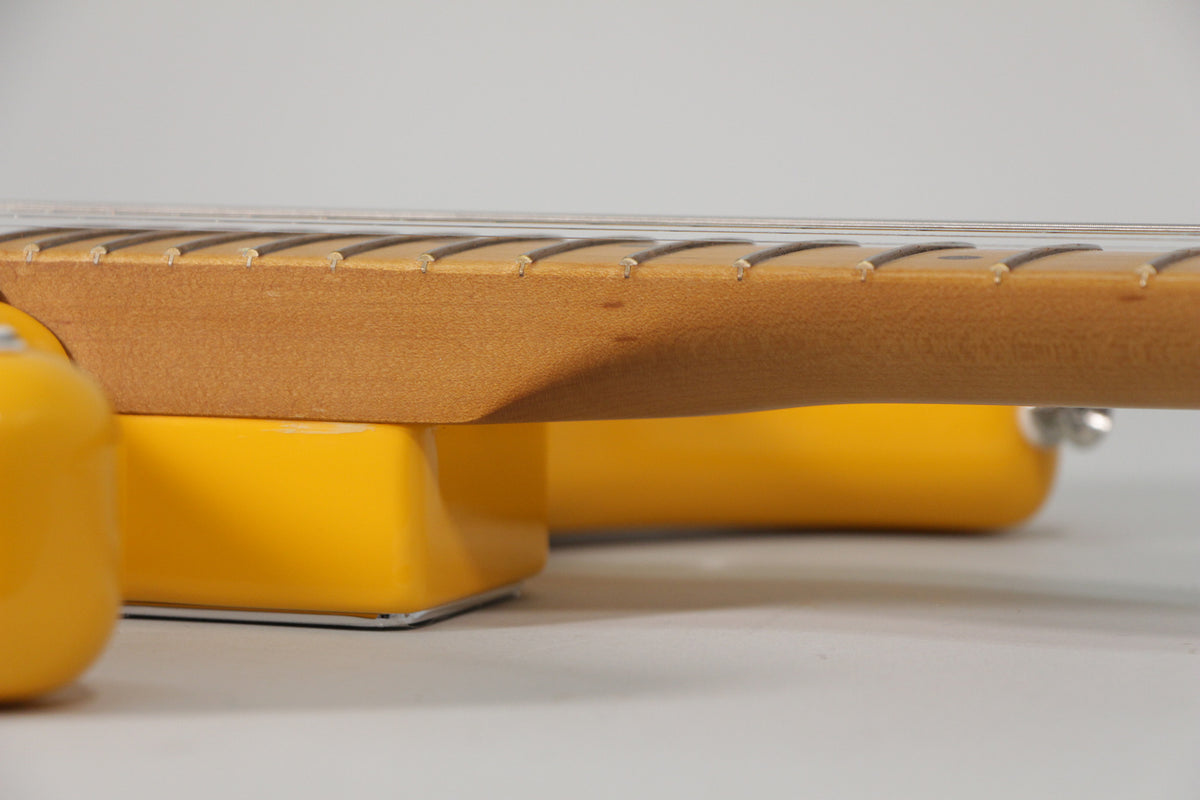 The guitar's maple neck and fretboard are visible from the side, with a slight ding on the neck and a vibrant yellow body.