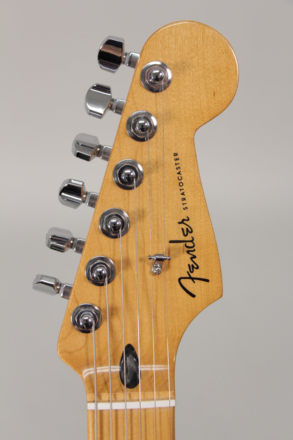 The guitar's headstock, with a natural wood finish, features six chrome tuning pegs and a black string tree.