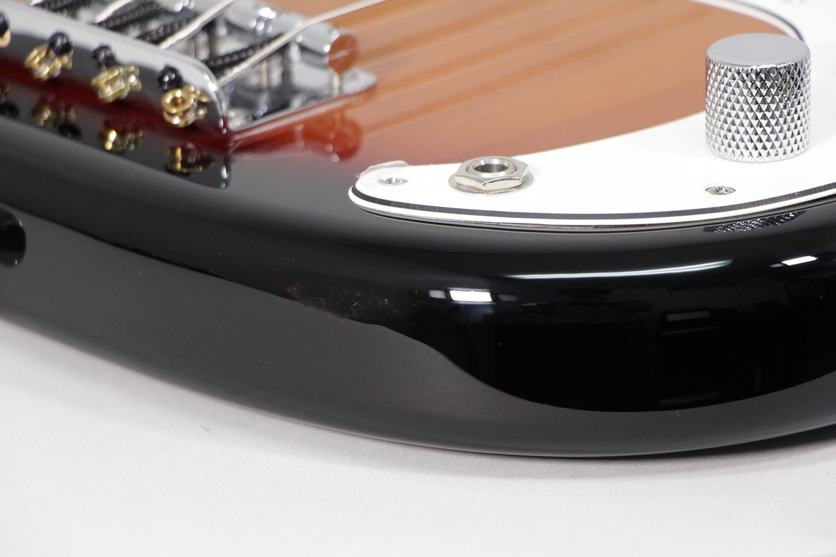 Close-up of the bass body's lower bout, showing the sunburst finish, white pickguard, chrome output jack, and a single knurled control knob.