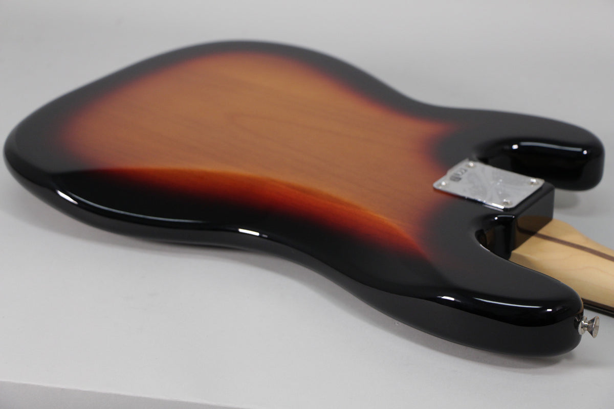 The bass guitar's sunburst body, with a glossy finish, is viewed from the back, showing the neck plate and strap button.