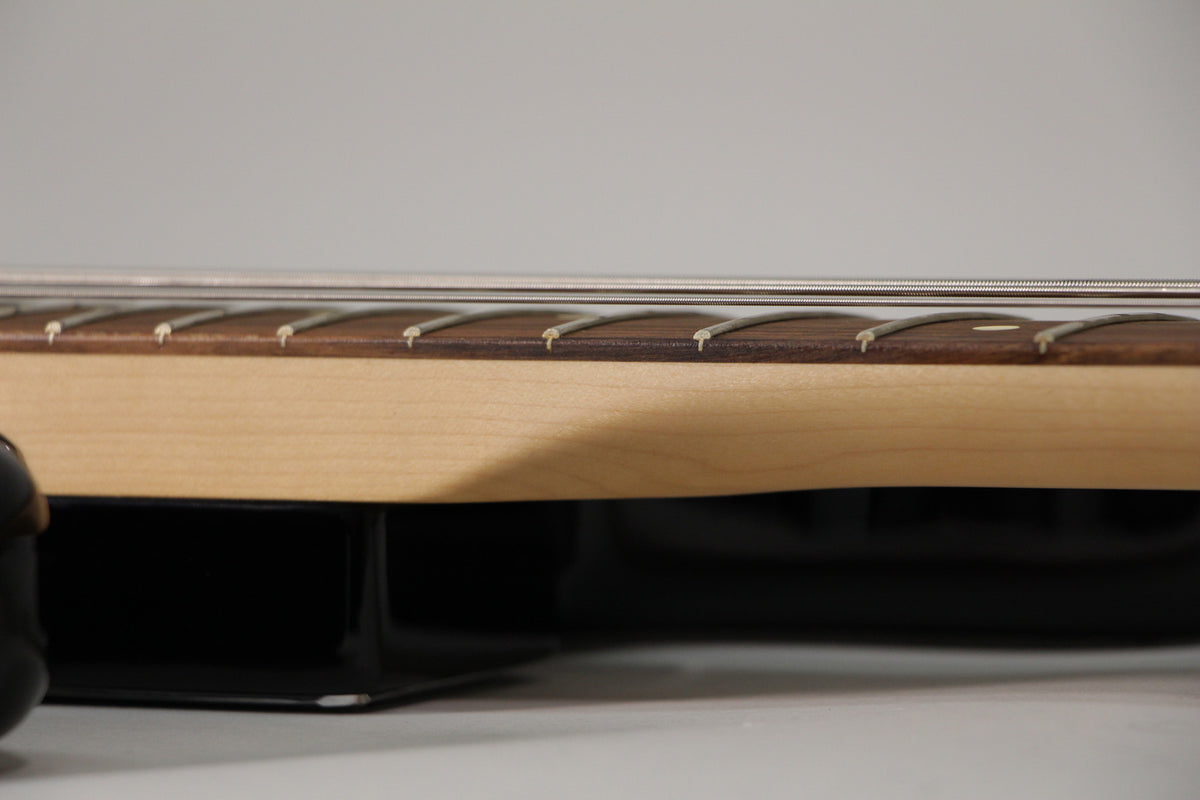 Close-up of the bass neck from the side, showing a light maple neck, dark fretboard with frets, and four strings.
