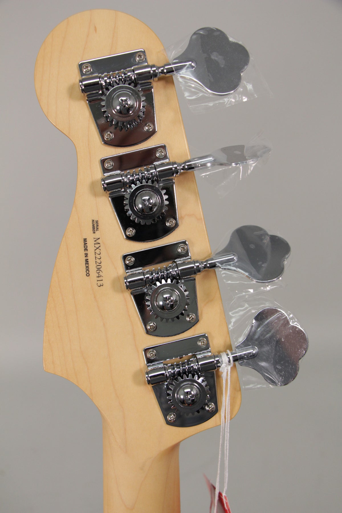 Rear view of the bass headstock, showing four chrome tuning machines with clover-leaf keys, some still in plastic wrapping.