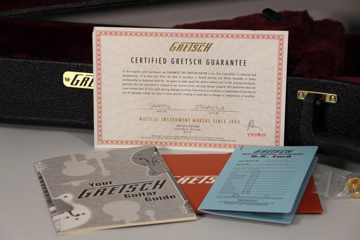 A close-up of the Gretsch Certified Guarantee, Guitar Guide, and O.K. Card, with the open hard case and its red plush interior visible.